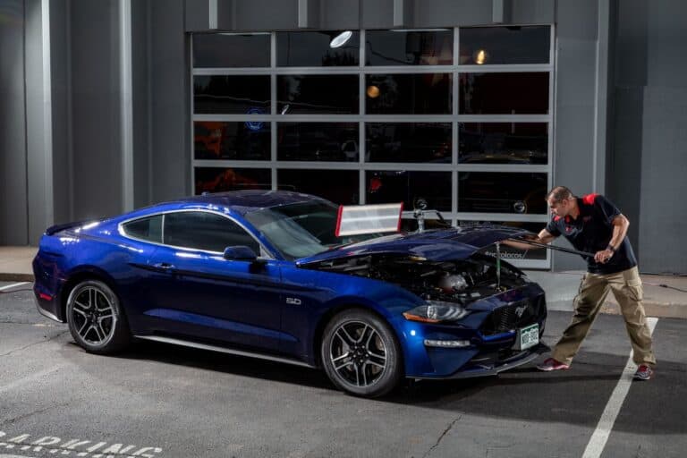 Technician inspecting a blue sports coupe for hail damage at RPM Dent Repair