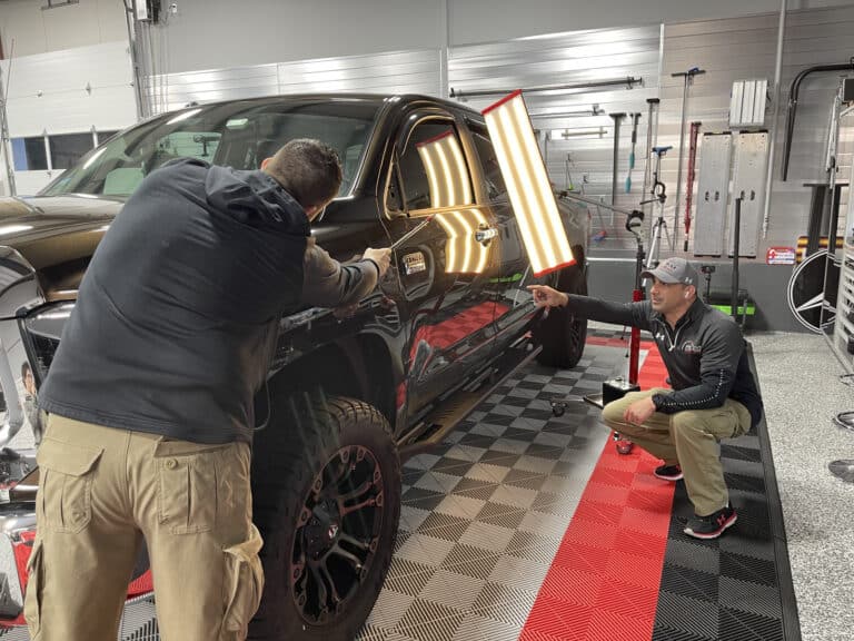 PDR technician using dent removal tools on vehicle panel in Raynham MA shop