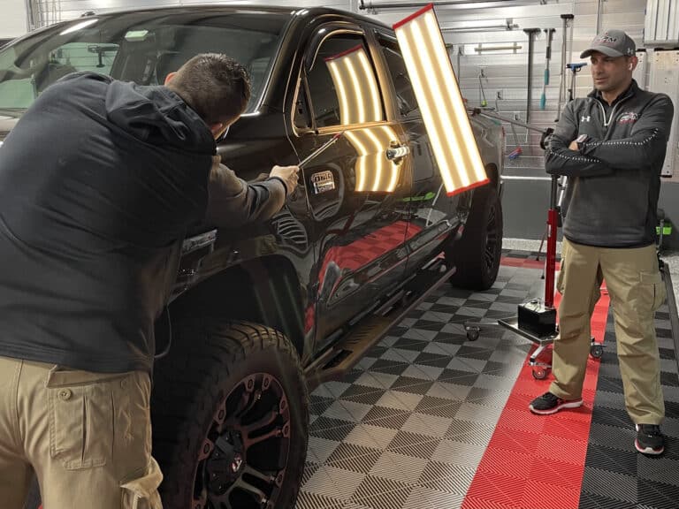 Paintless dent repair technician working on car body panel inside RPM Dent Repair shop Raynham MA